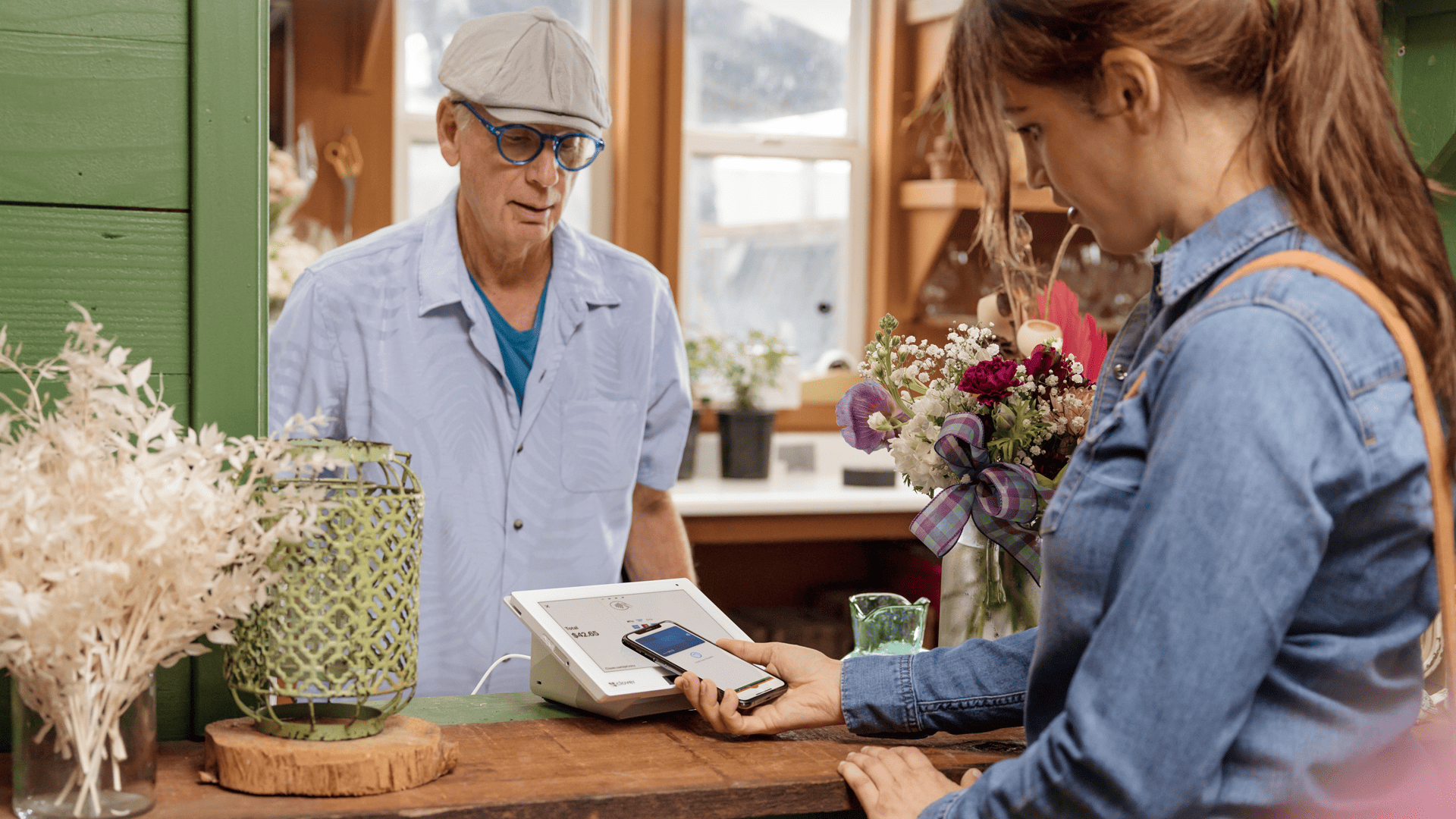 Cliente realizando pago móvil sin contacto en una floristería con smartphone y terminal POS.